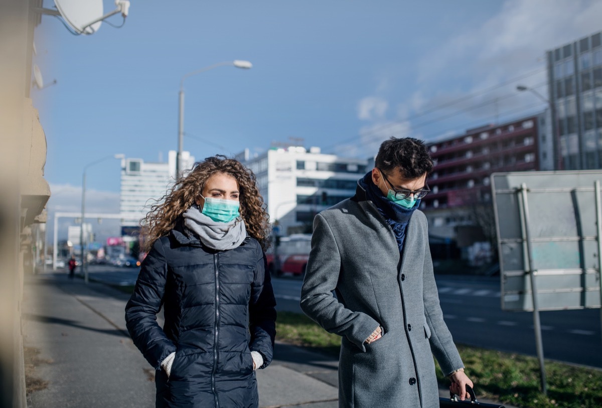 white woman and man walking in face masks in a city