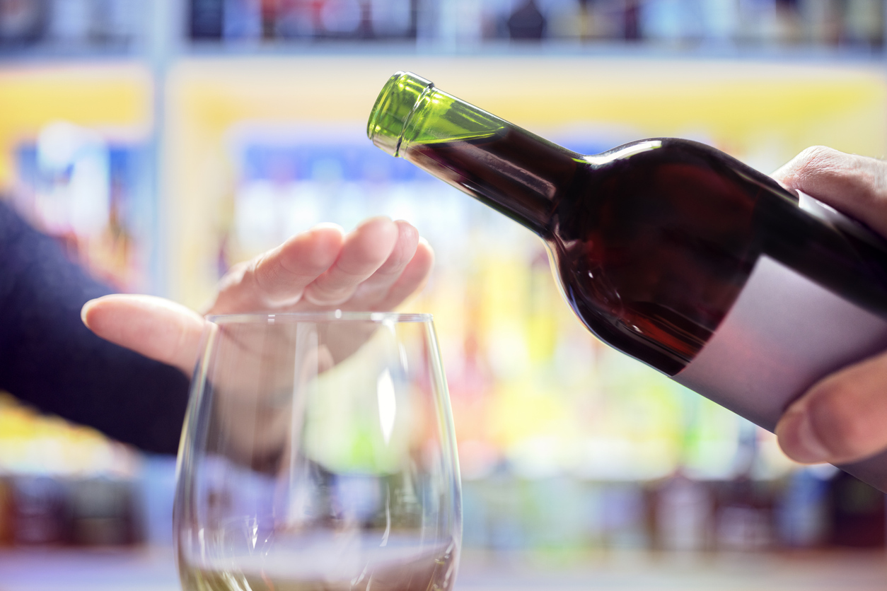 Bottle of wine tipped towards empty glass with hand blocking it. 