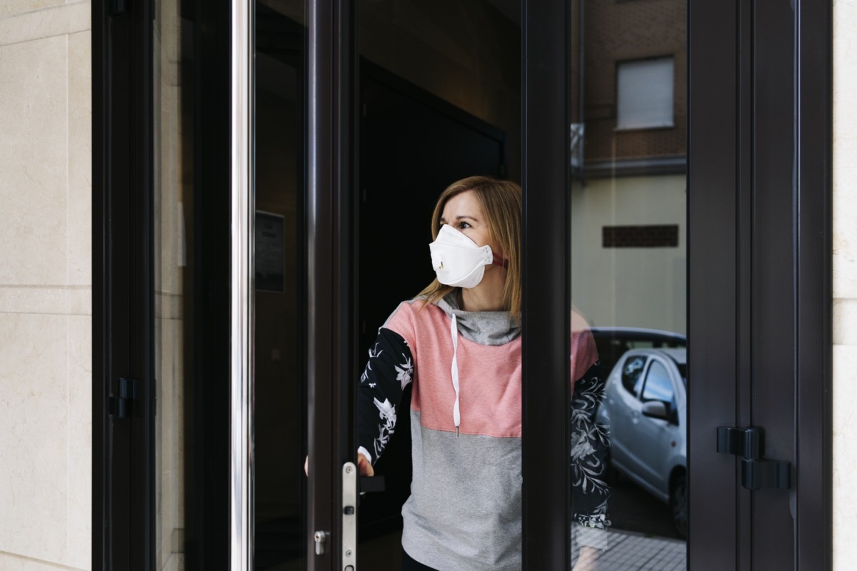 Woman goes out to the street from the door of her house with a face mask