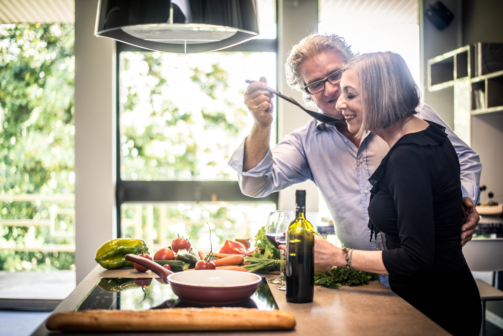 A senior couple standing in the kitchen and trying a taste over the stove