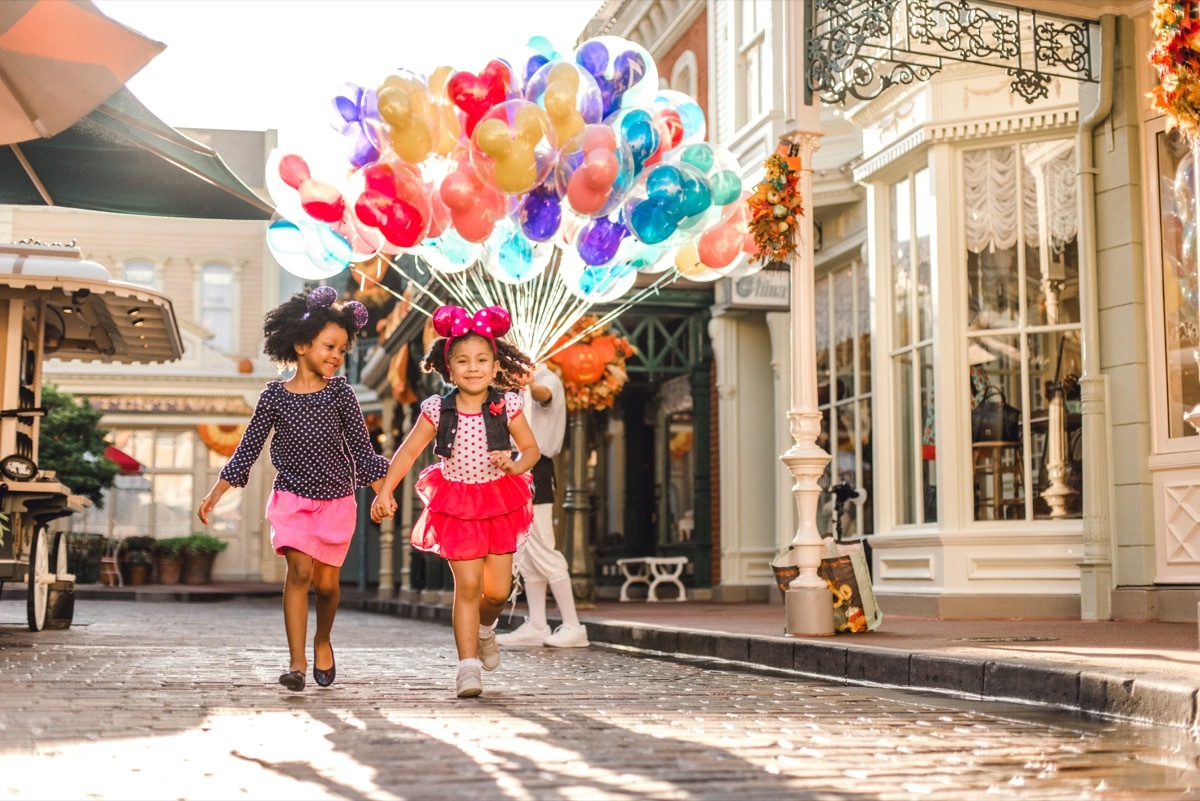 two girls with mickey mouse ears carry a bunch of balloons