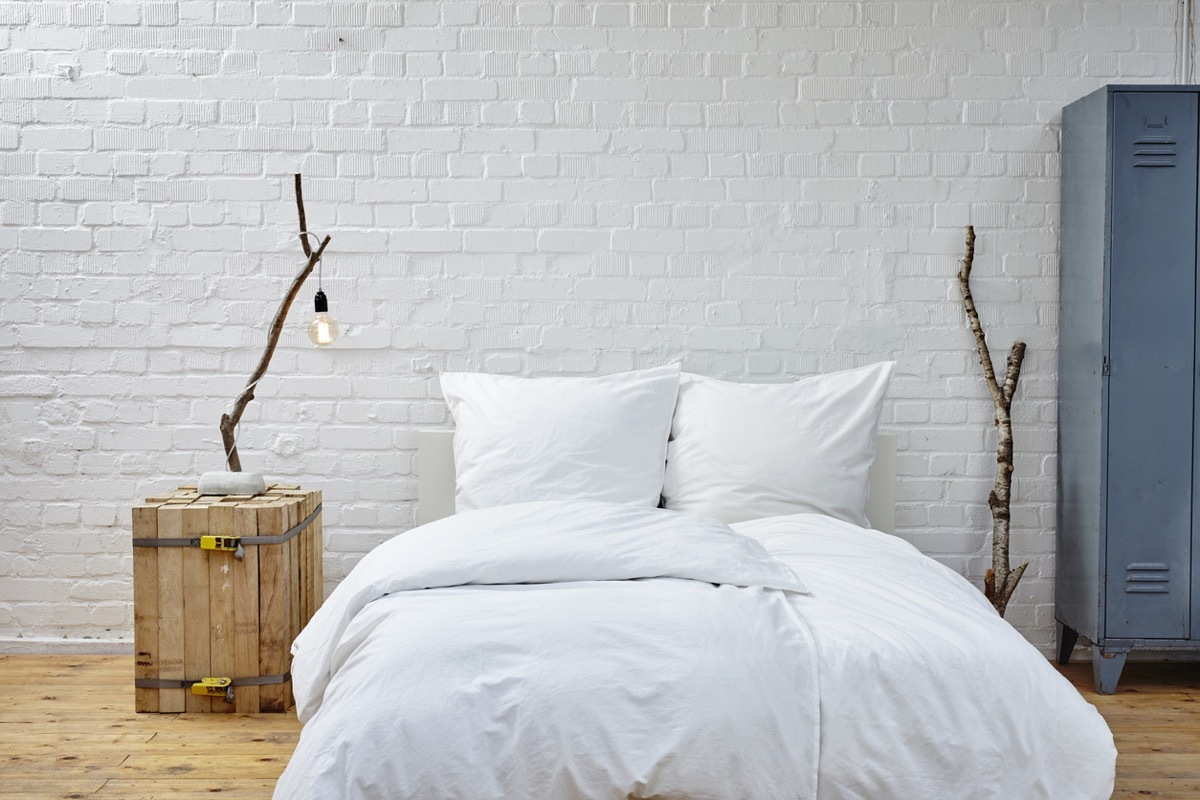 white bed on floor with white brick wall behind it and wooden nightstand