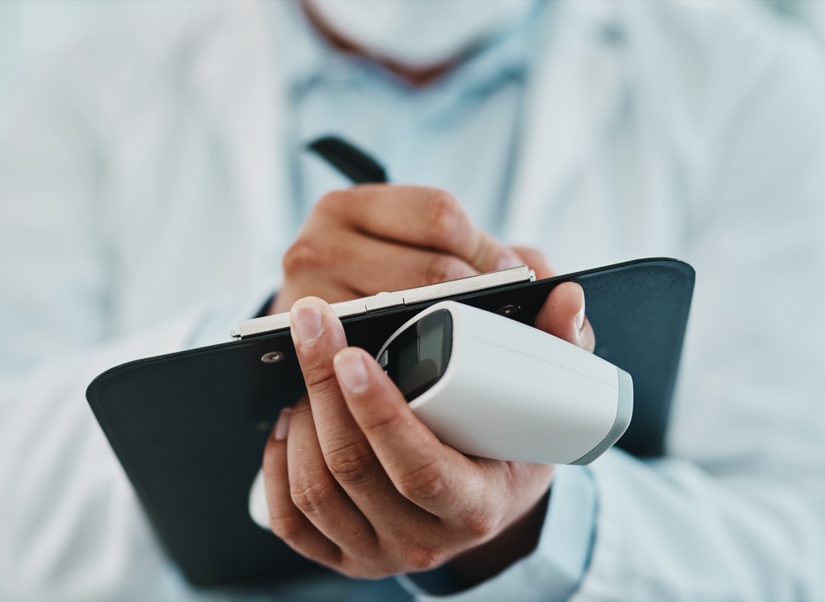 Cropped shot of a doctor holding an infrared thermometer and writing notes during an outbreak