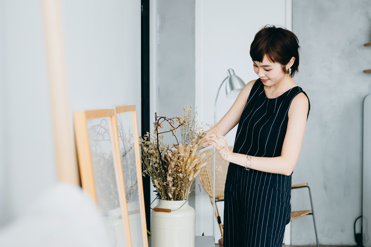 Young Asian woman decorating and arranging a vase with dried plants on cabinet in the living room at home