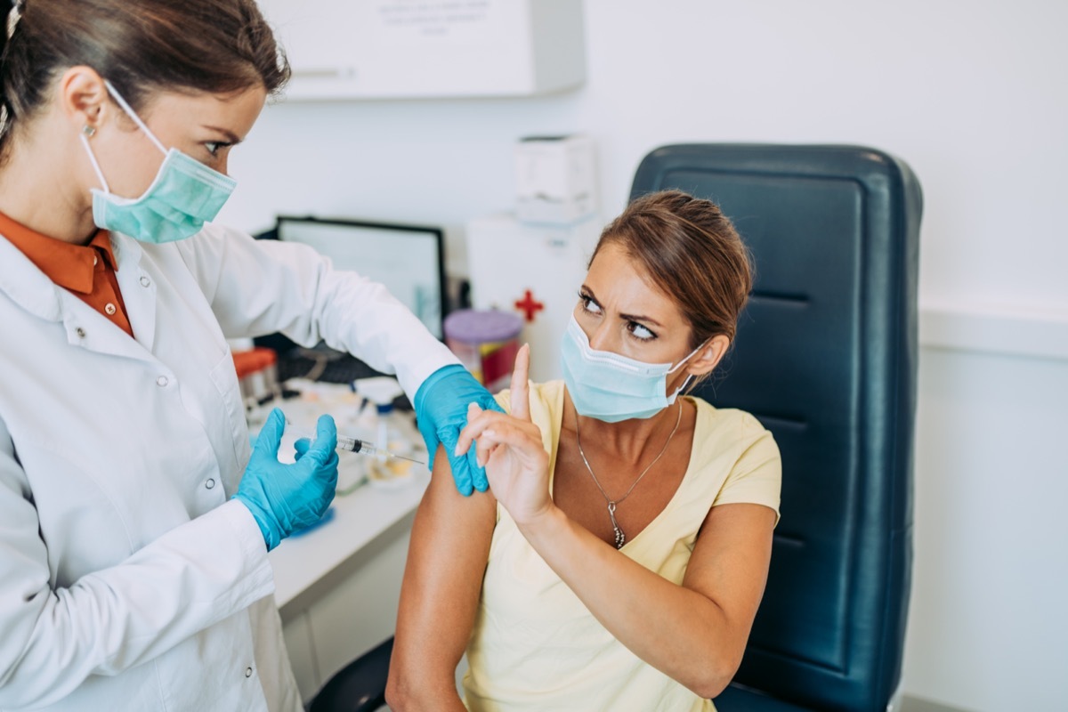 Female doctor or nurse trying to give shot or vaccine against virus to a scared patient. Angry and distrustful patient refuses to receive it.