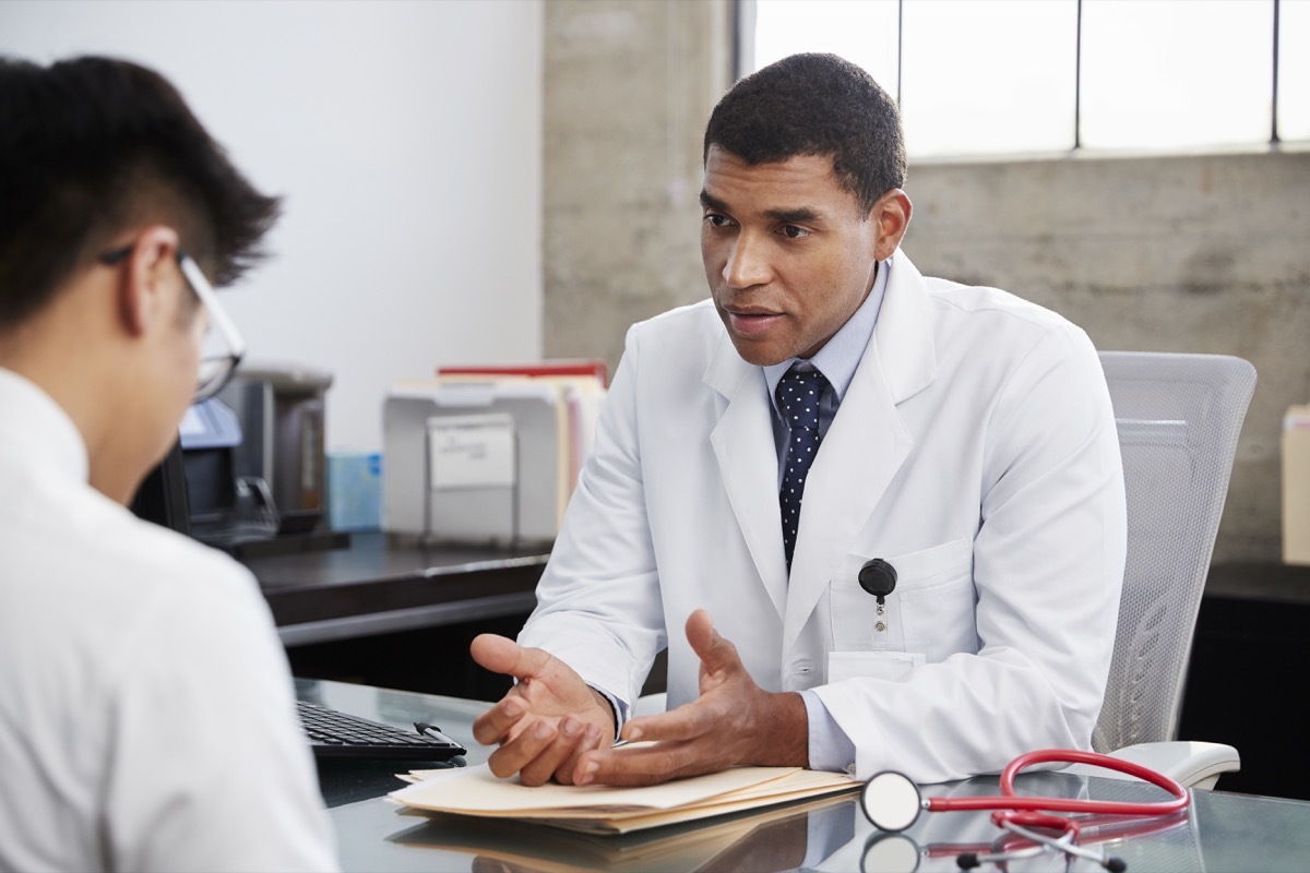 doctor in a white coat, speaking to a patient at a desk