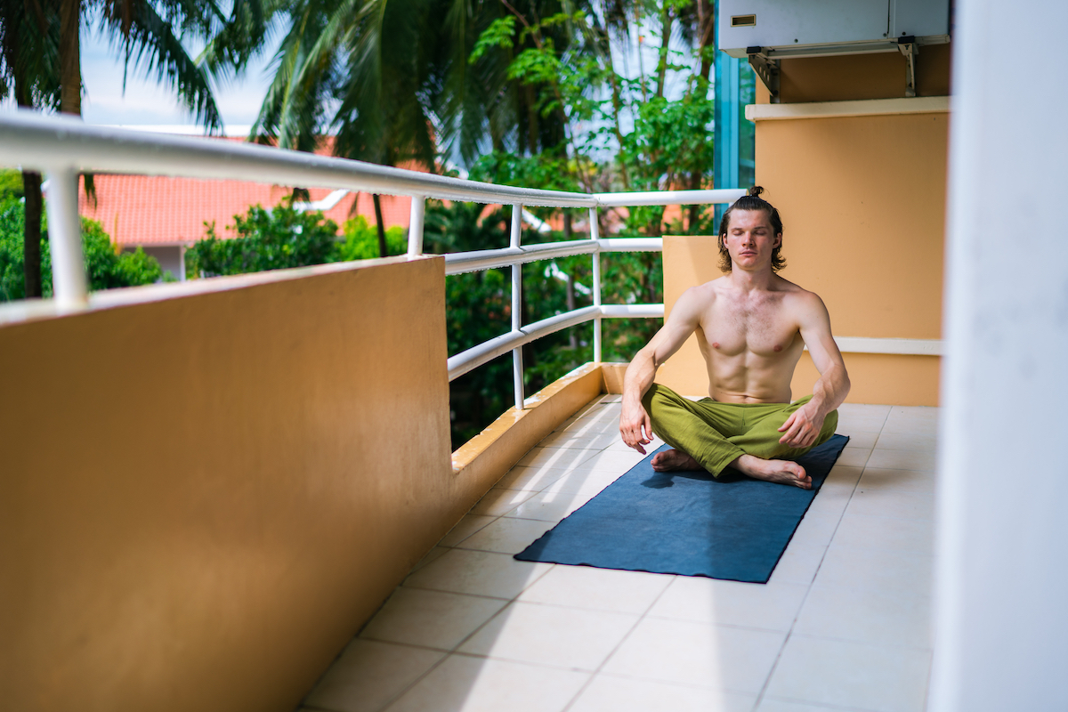 Handsome man practicing yoga on a balcony at home. Male yogi sitting on mat in meditation