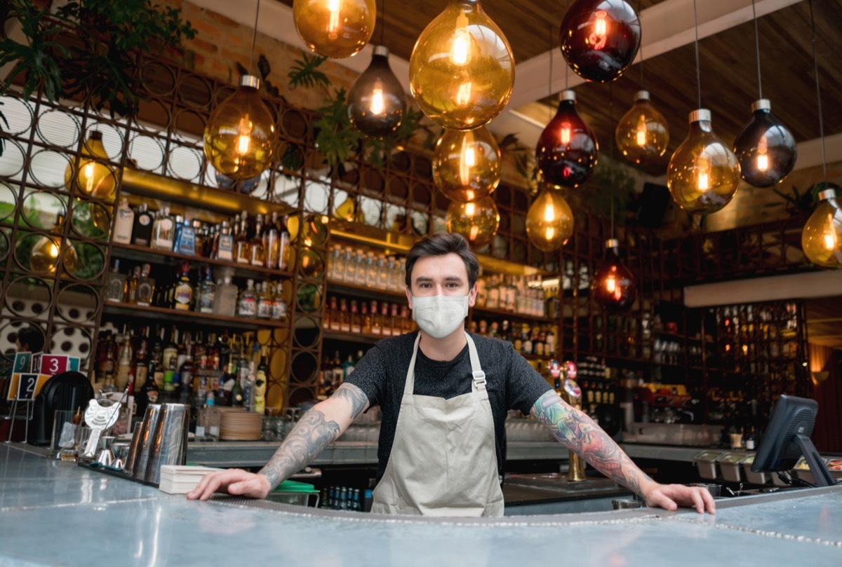 Happy bartender working at a bar wearing a face mask.