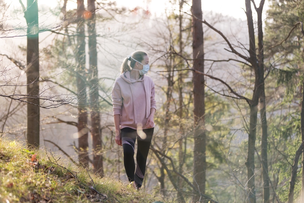 Portrait of sporty woman wearing a medical protection face mask while walking in the forest. Corona virus, or Covid-19, is spreading all over the world.