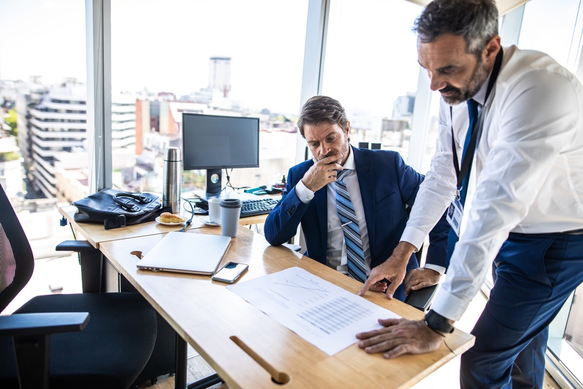 Male colleagues cooperating on their project in co-working office, looking at paper documents together