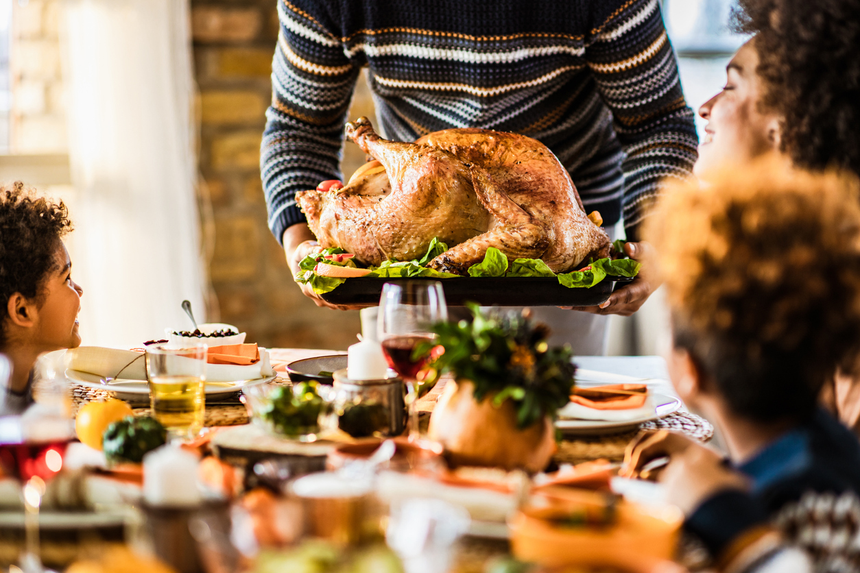 A person placing a Thanksgiving turkey down on the table in front of their family