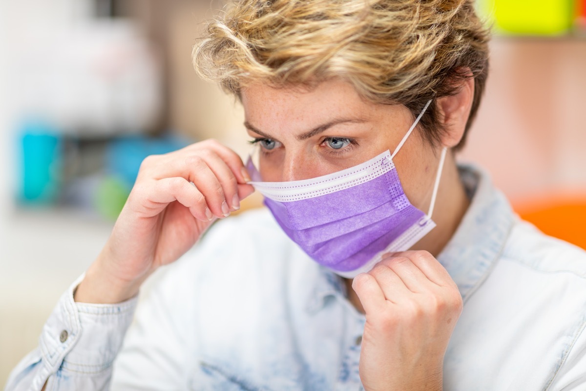 Middle aged employee fitting protective mask on her face