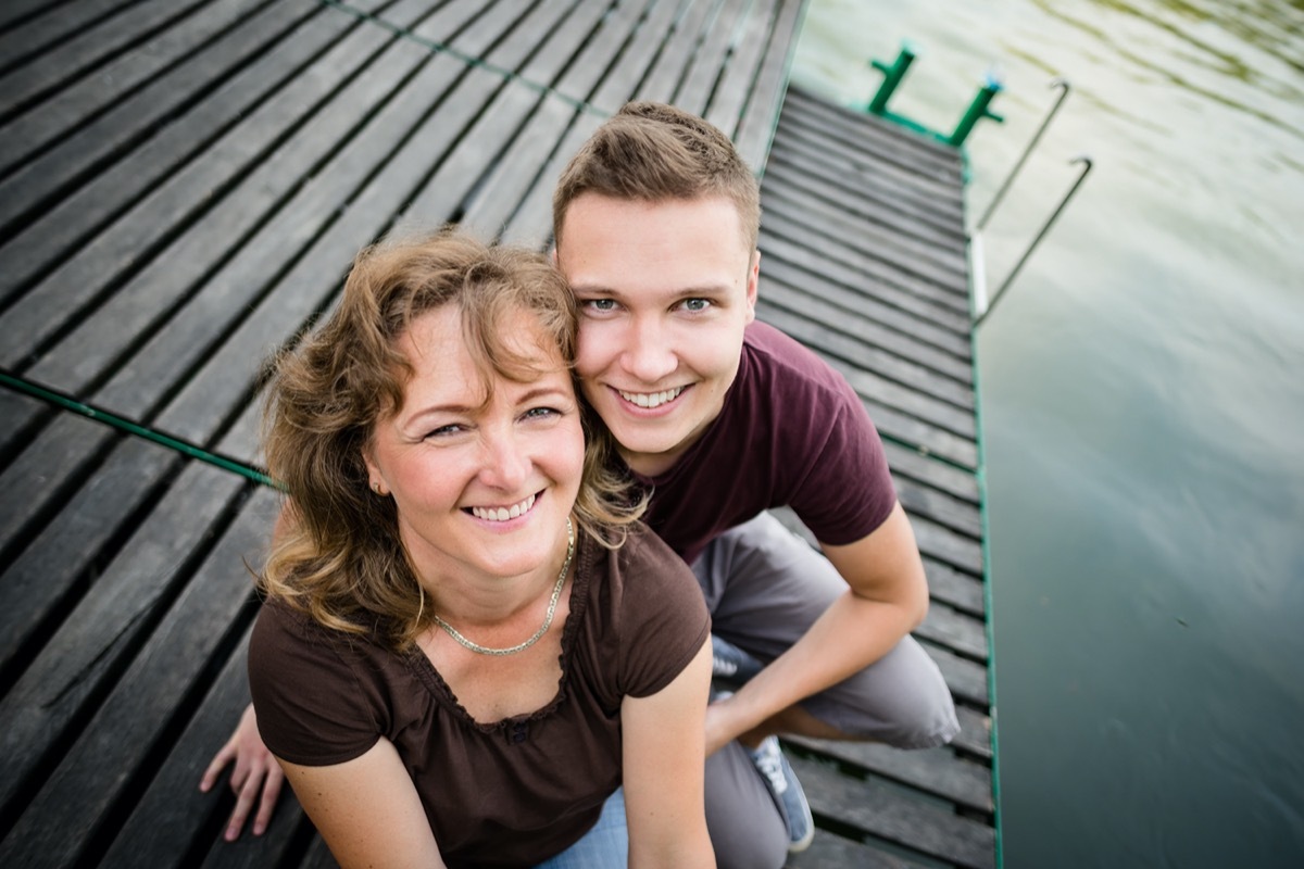 Mother with her adult son sitting on a wooden pier near forest lake.