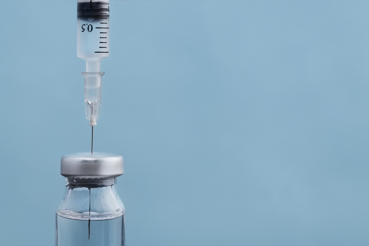 syringe dipped into vial of vaccine on blue background