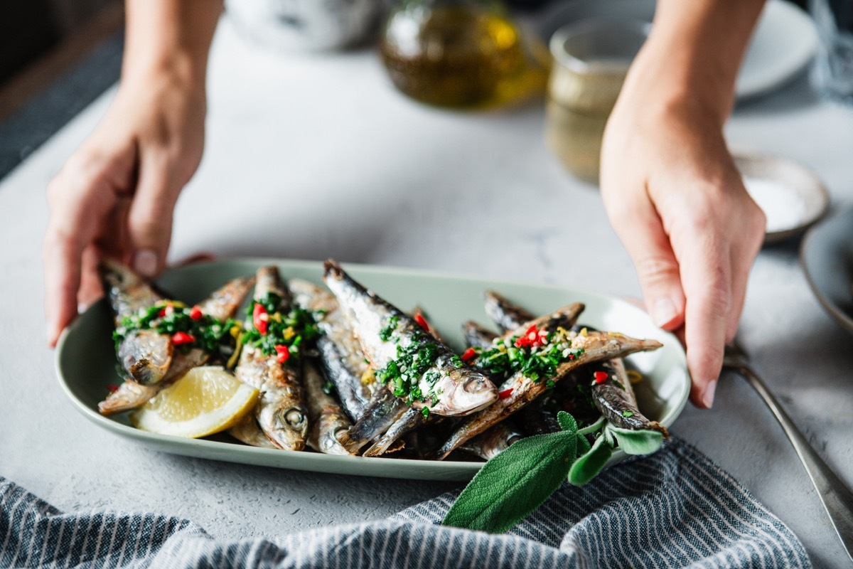 Woman's hand serving fried fish with lemon on dining table. Close-up of a female placing freshly cooked seafood on table.