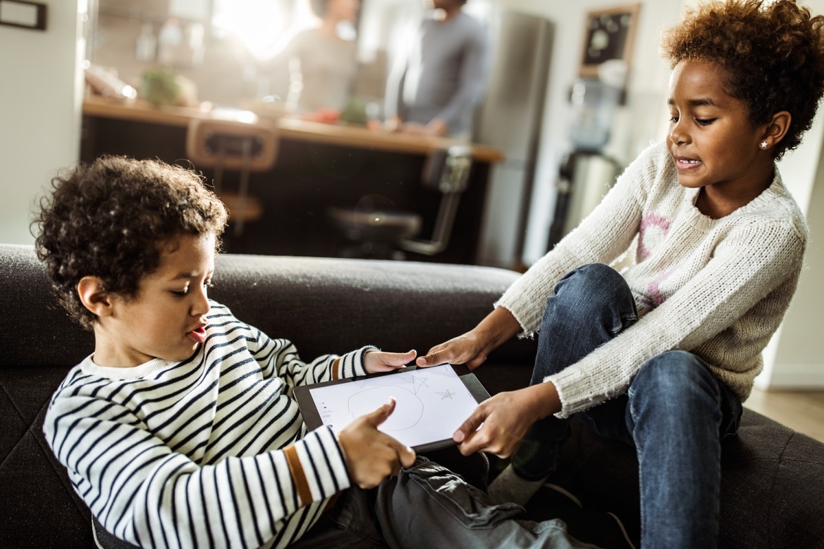 two small children fighting over an ipad on their living room couch