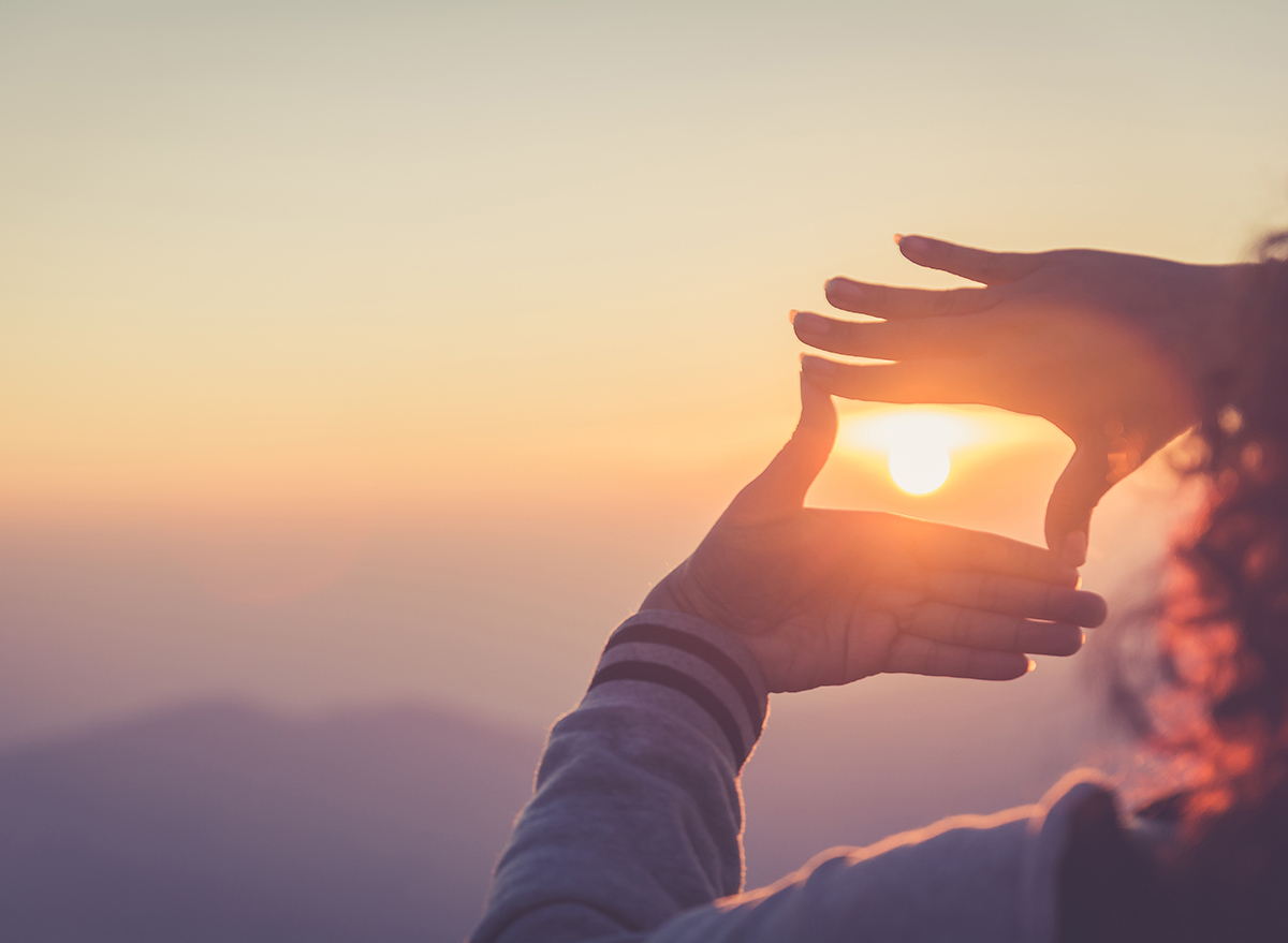 person makes a picture frame with hands around the sun as it sets