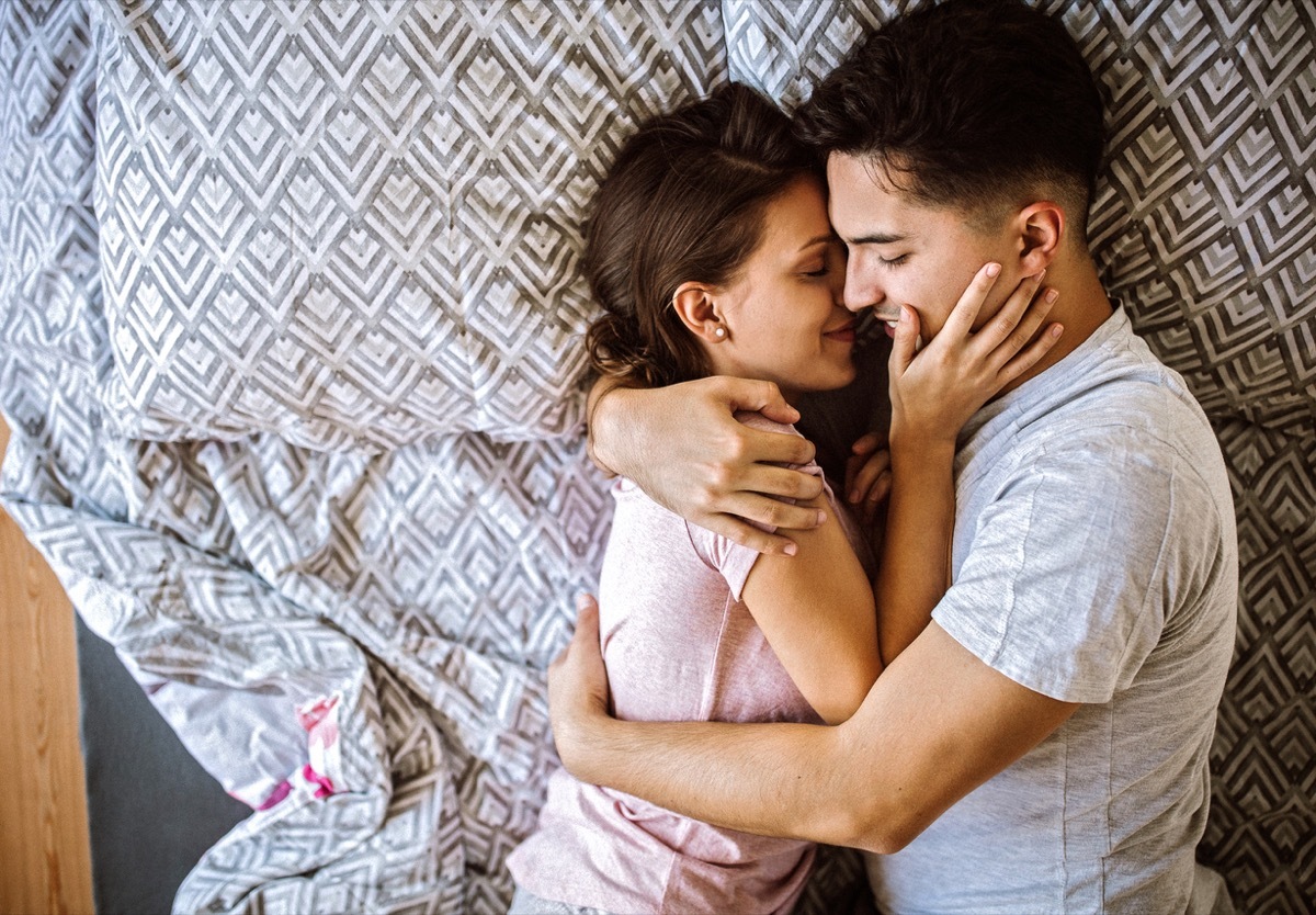 Young couple in love lying on bed at home and cuddling, embracing and enjoying weekend together