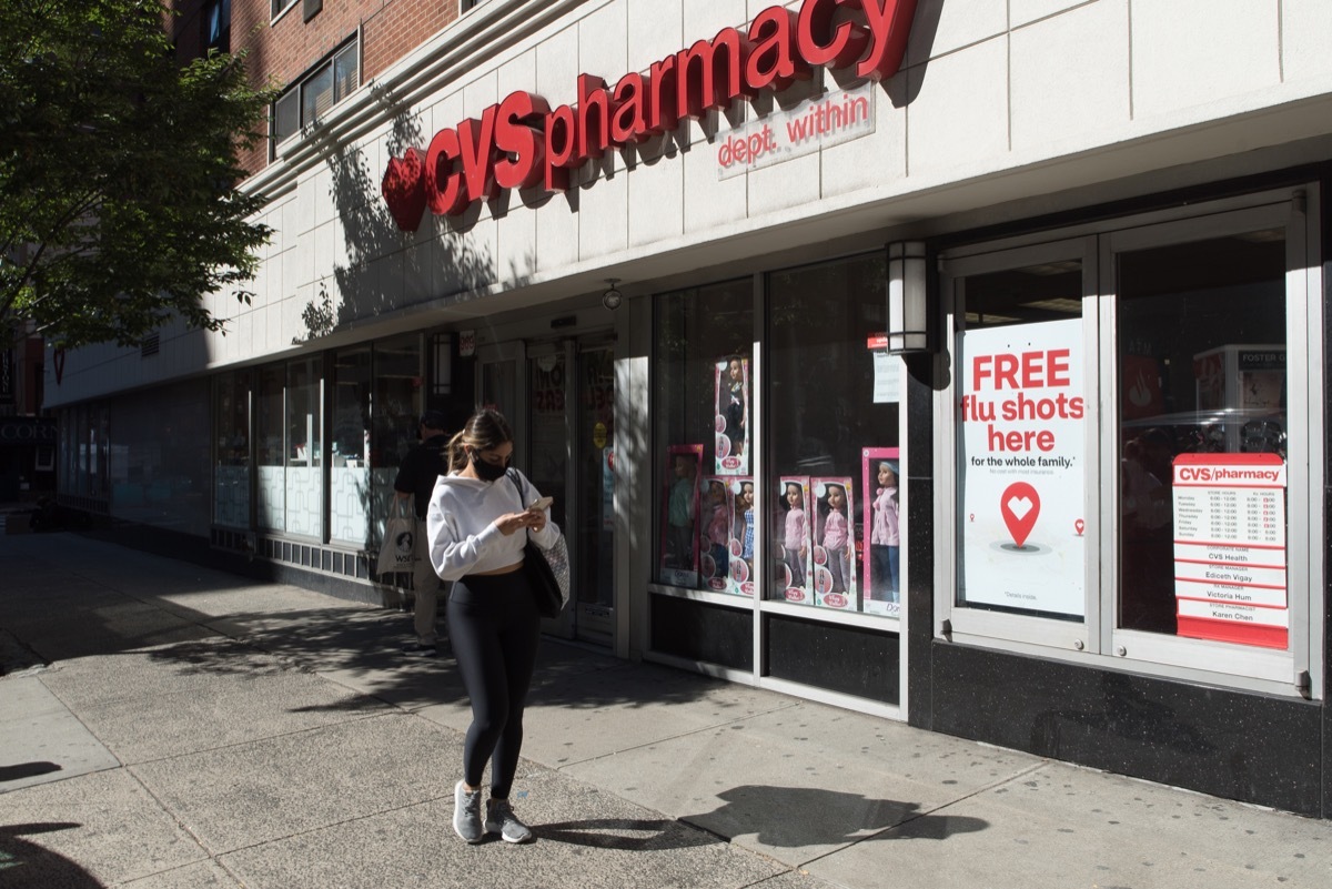 Manhattan, New York. October 08, 2020. A woman wearing a face mask walks in front of a CVS pharmacy Midtown with a sigh advertising free flu shots.