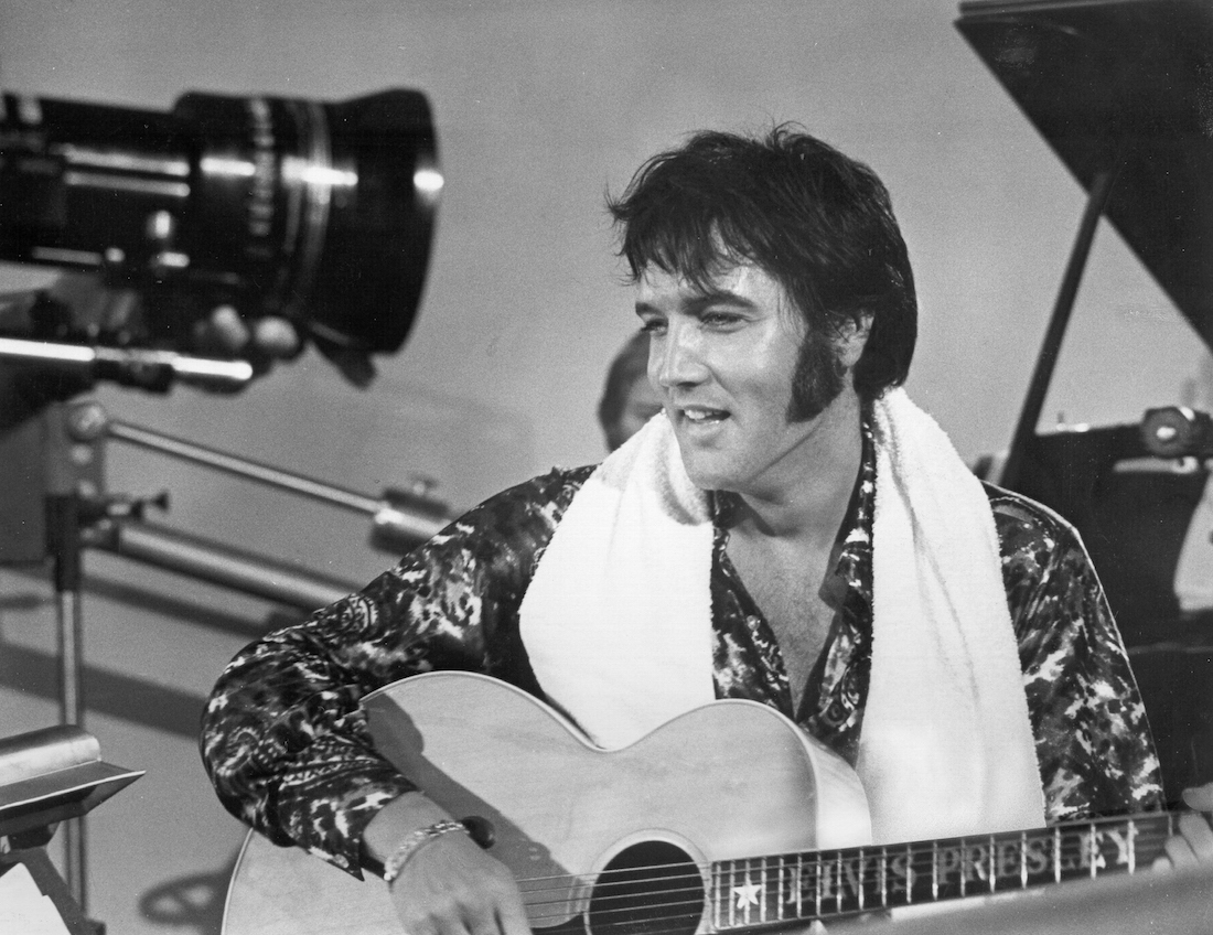 Elvis Presley holding an acoustic guitar in front of a TV camera circa 1973