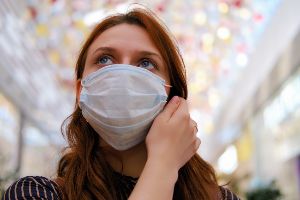 A young woman is considering whether to remove the medical mask after the end of the quarantine due to the coronavirus.