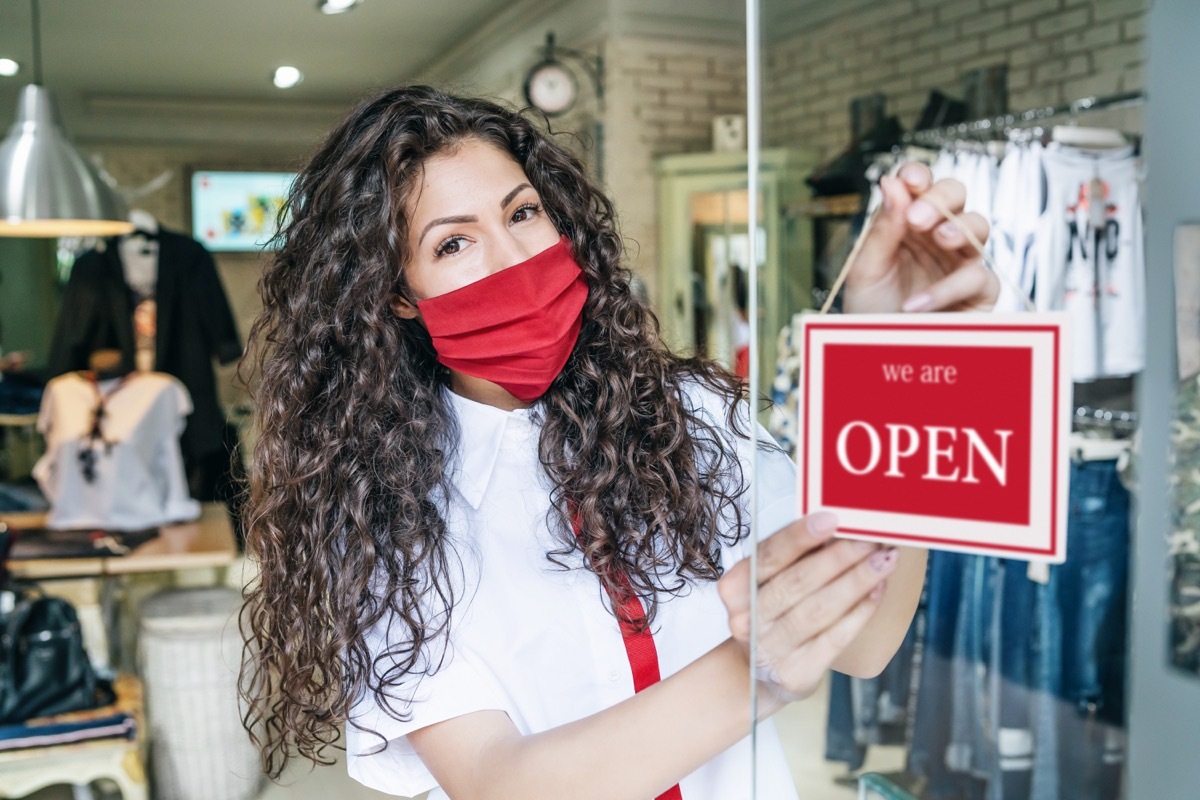 Happy business owner hanging an open sign during COVID-19