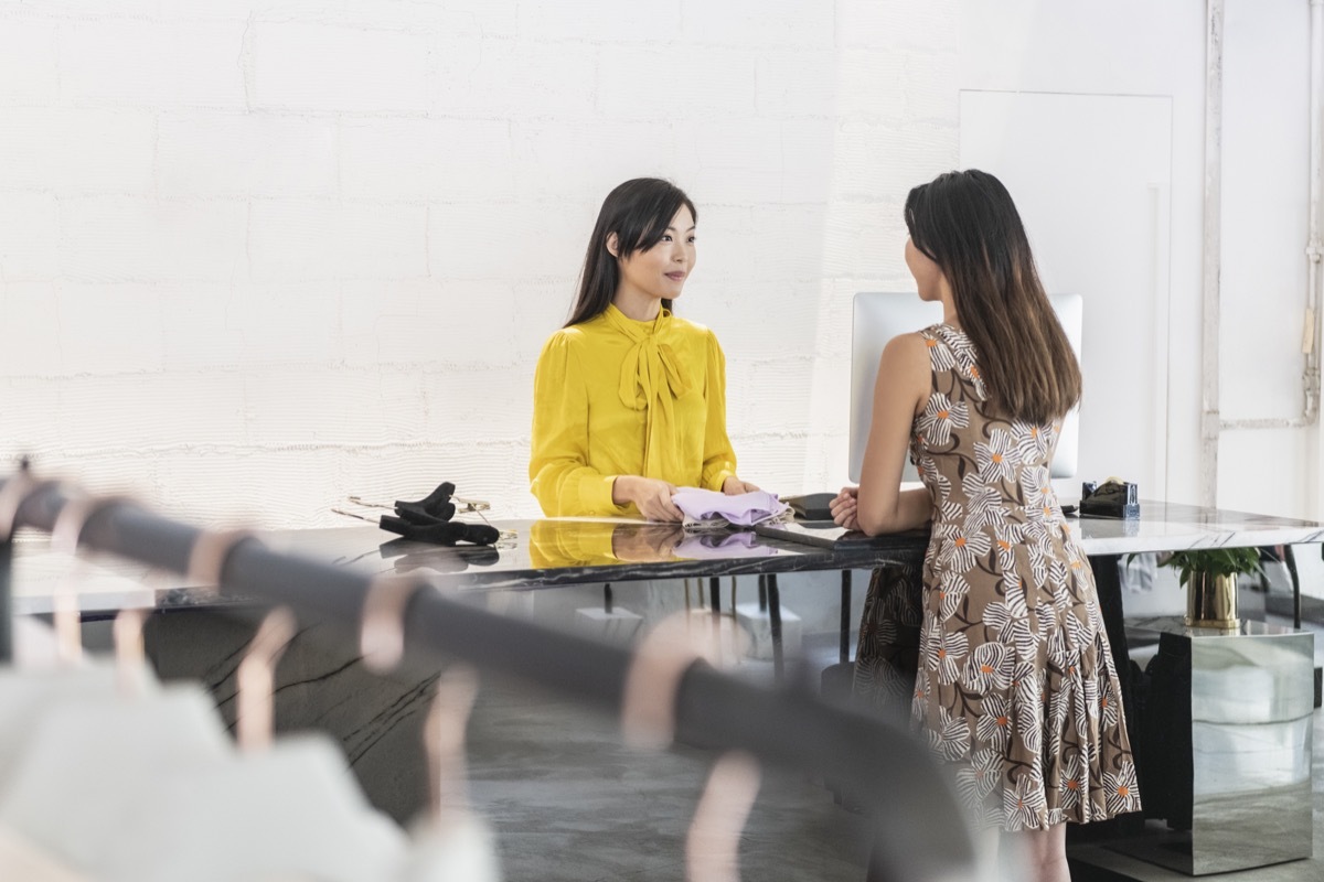 Young woman in floral dress standing at counter and discussing with shop worker, buying clothed, service, consumer rights, decisions getting money back instantly