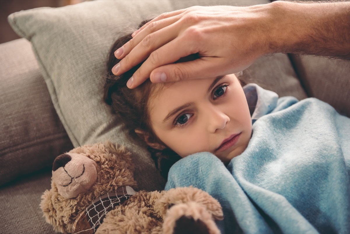 Sick little girl covered in blanket is lying on couch