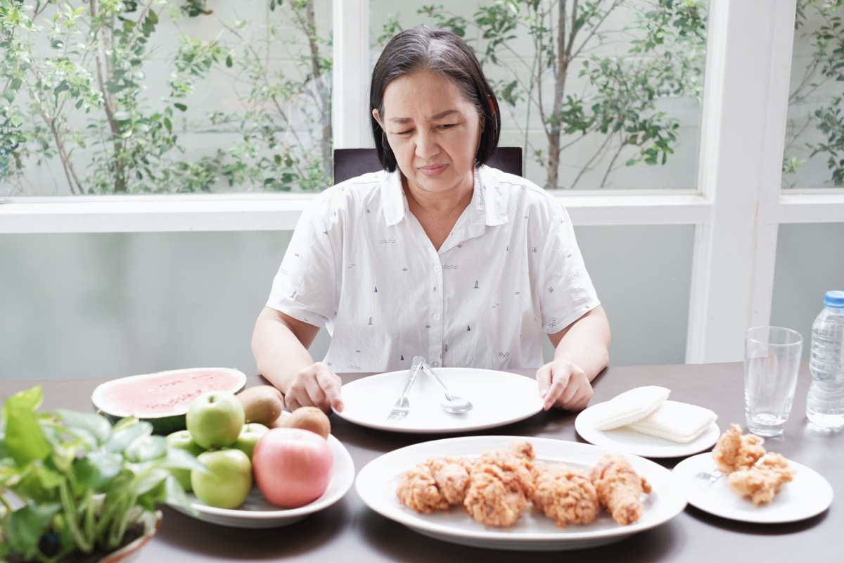 older woman sitting at table with plates of food but not eating