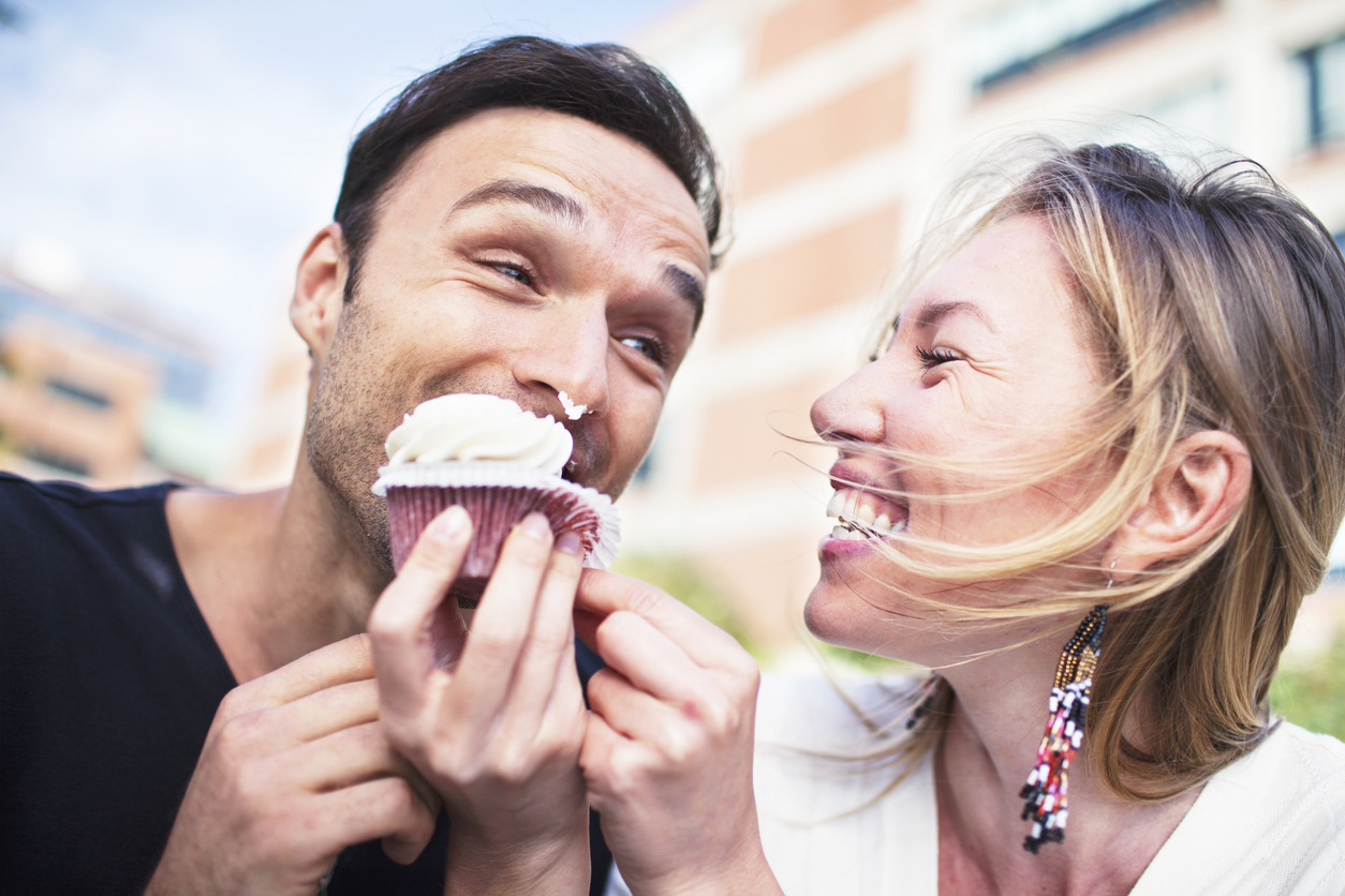 Joyful couple eating cupcake outdoors