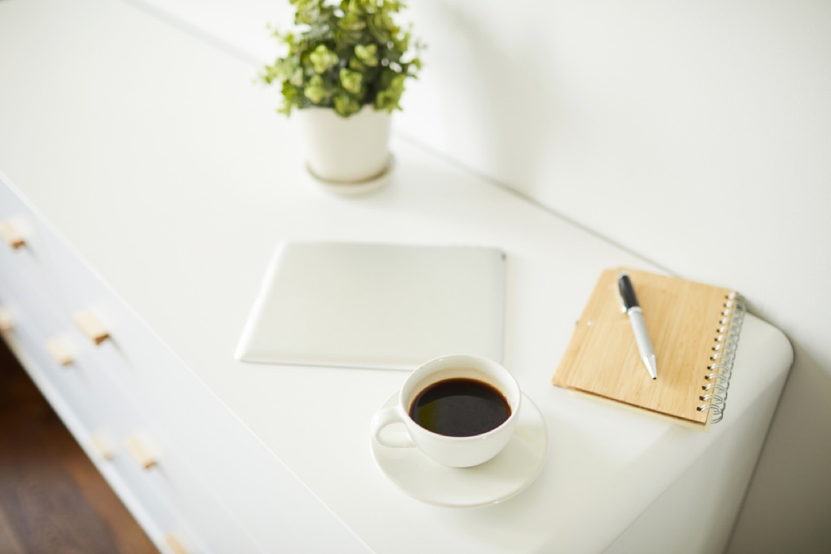 white nightstand with notebook, coffee, tablet, and plant on it