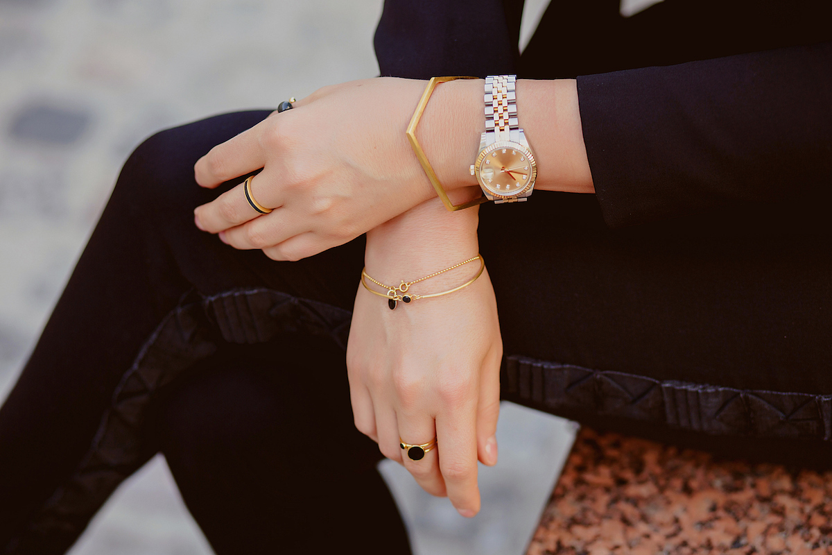 Close up of a woman dressed in black with her legs crossed wearing multiple rings and bracelets