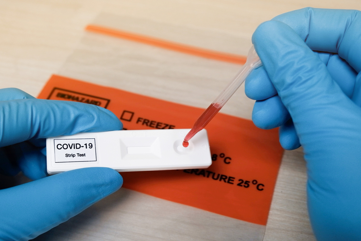 A close up of a technician wearing blue gloves placing a drop of blood on a COVID-19 antibody test strip