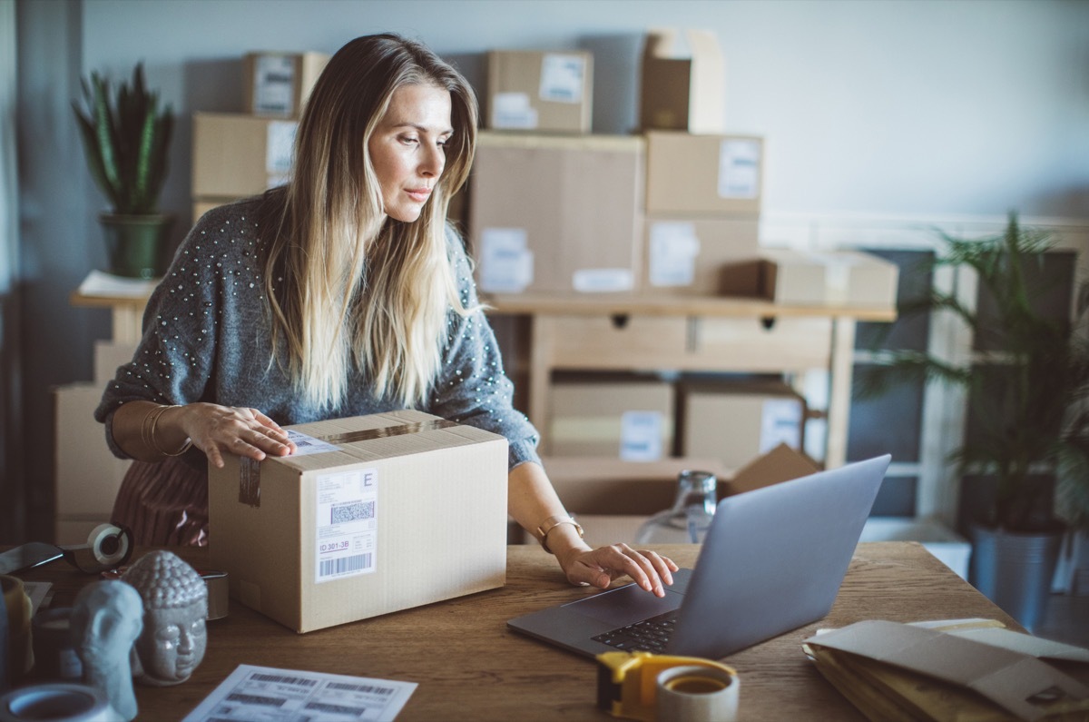 Working woman at online shop. She wearing casual clothing and checking on laptop address of customer and package information