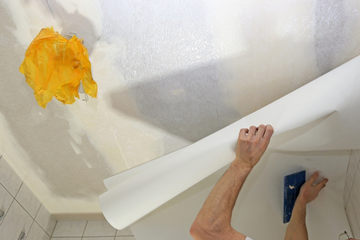 man wallpapering ceiling with white paper