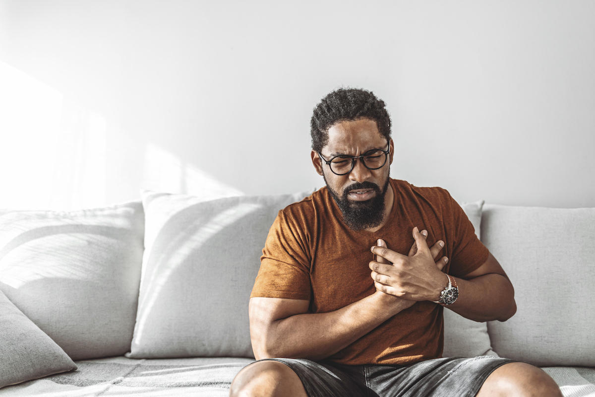 Man with high blood pressure experiencing chest pain while sitting at home during the day.