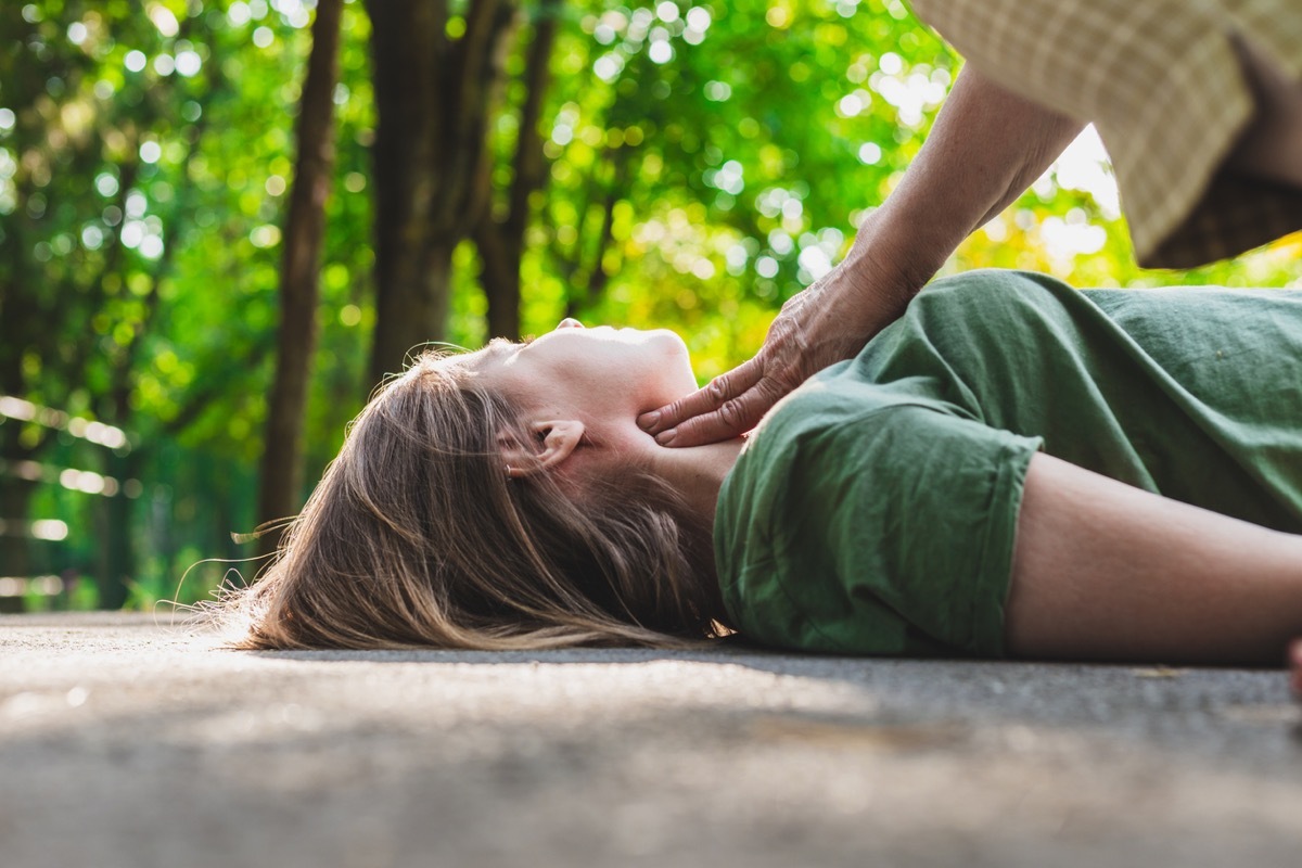 unconscious fainted girl having pulse checked by an old woman - Teenager lying on the ground while her pulse is verified by an elder citizen on teen's carotid artery (Unconscious fainted girl having pulse checked by an old woman - Teenager lying