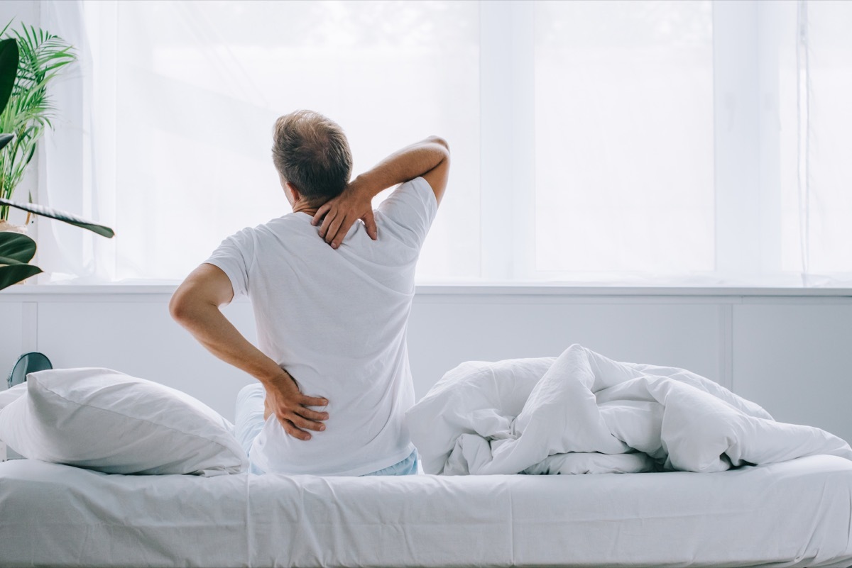 man with back pain sitting on a bed, signs you need a new mattress