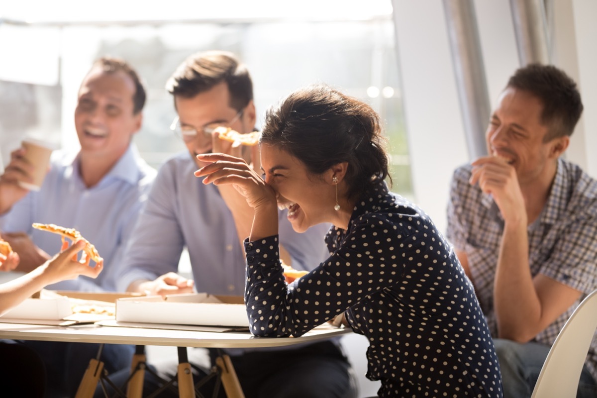 One woman and three men laughing and sharing pizza