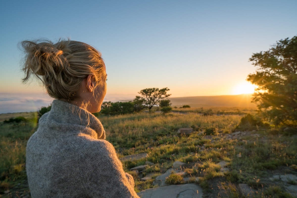 woman watching sunset outside with trees and grass around her