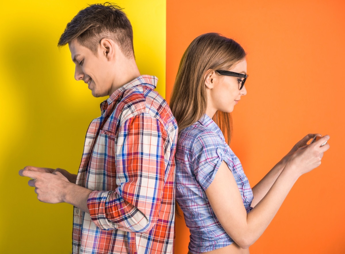 Portrait of young couple standing back to each other and looking at the phone.