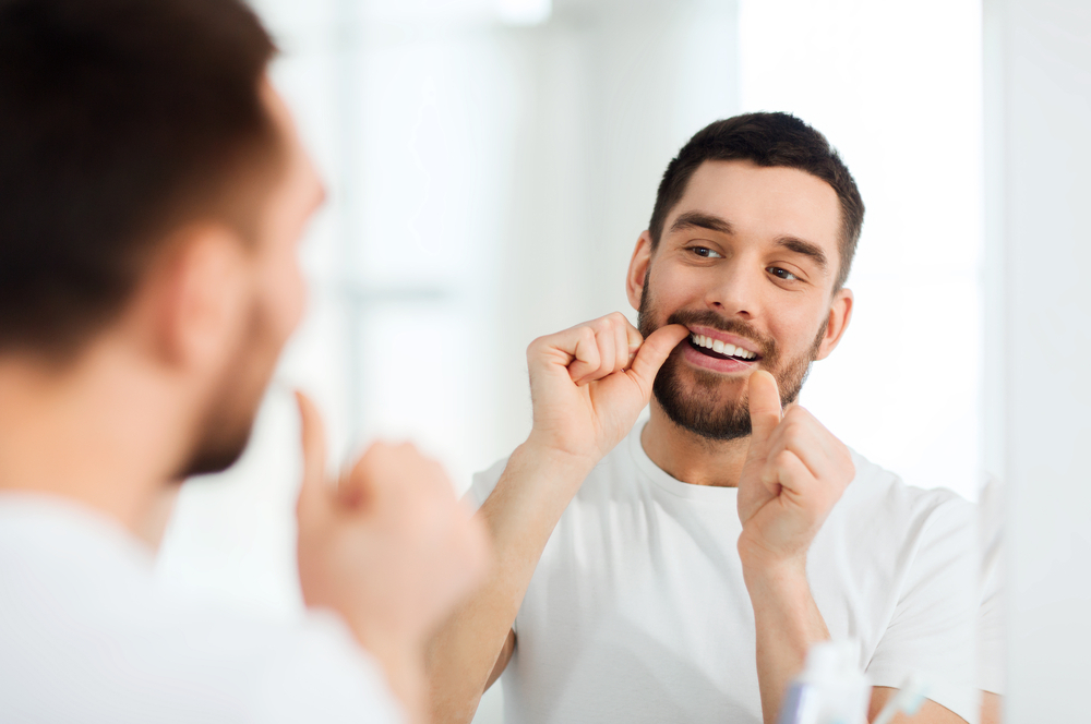 man flosses while looking in mirror