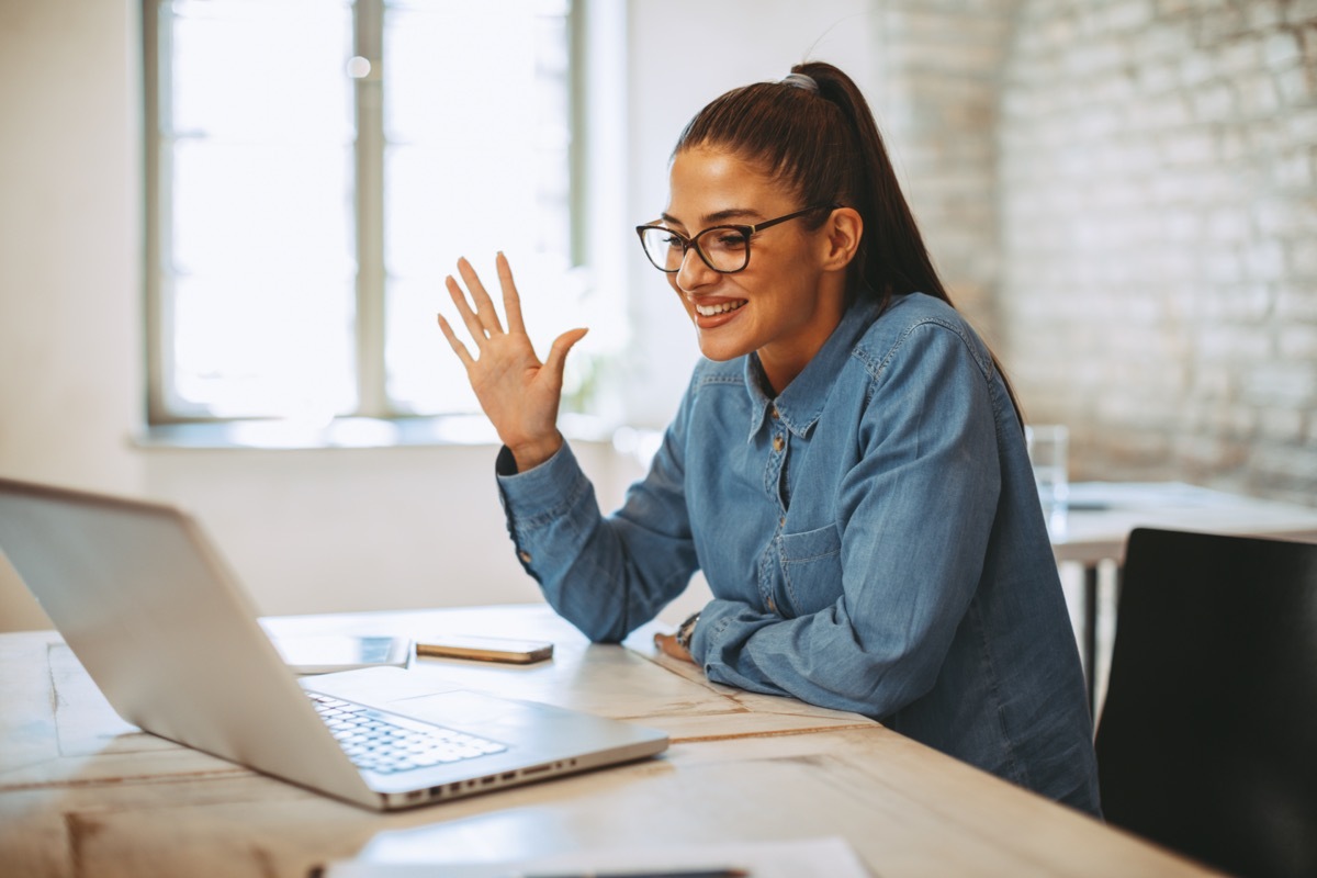 young woman in glasses waving to her laptop