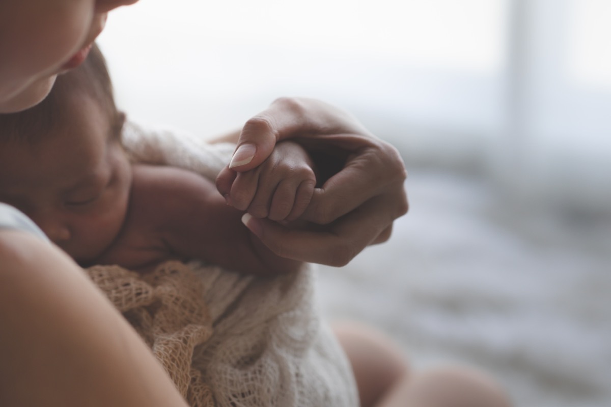 Close up Mother holding hands Asian female newborn baby and sunlight in the morning. Cute little girl three weeks old. Health, care, love, relationship concept.