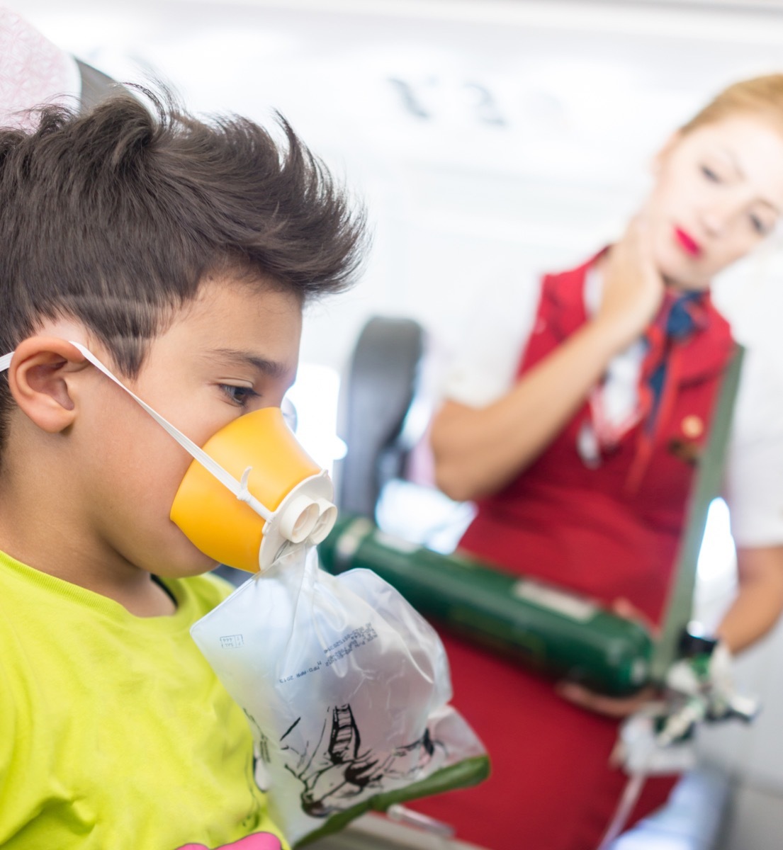 boy in airplane seat with oxygen mask as flight attendant looks on, annoyed flight attendant