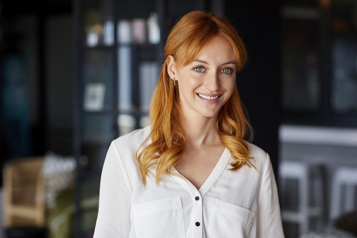 A young pretty woman with red hair smiling at the camera, wearing a white blouse