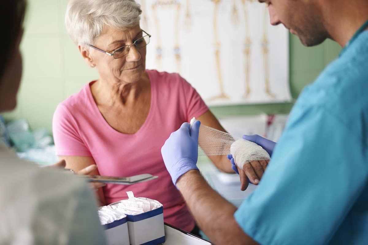 white doctor bandaging the hand of an older white woman