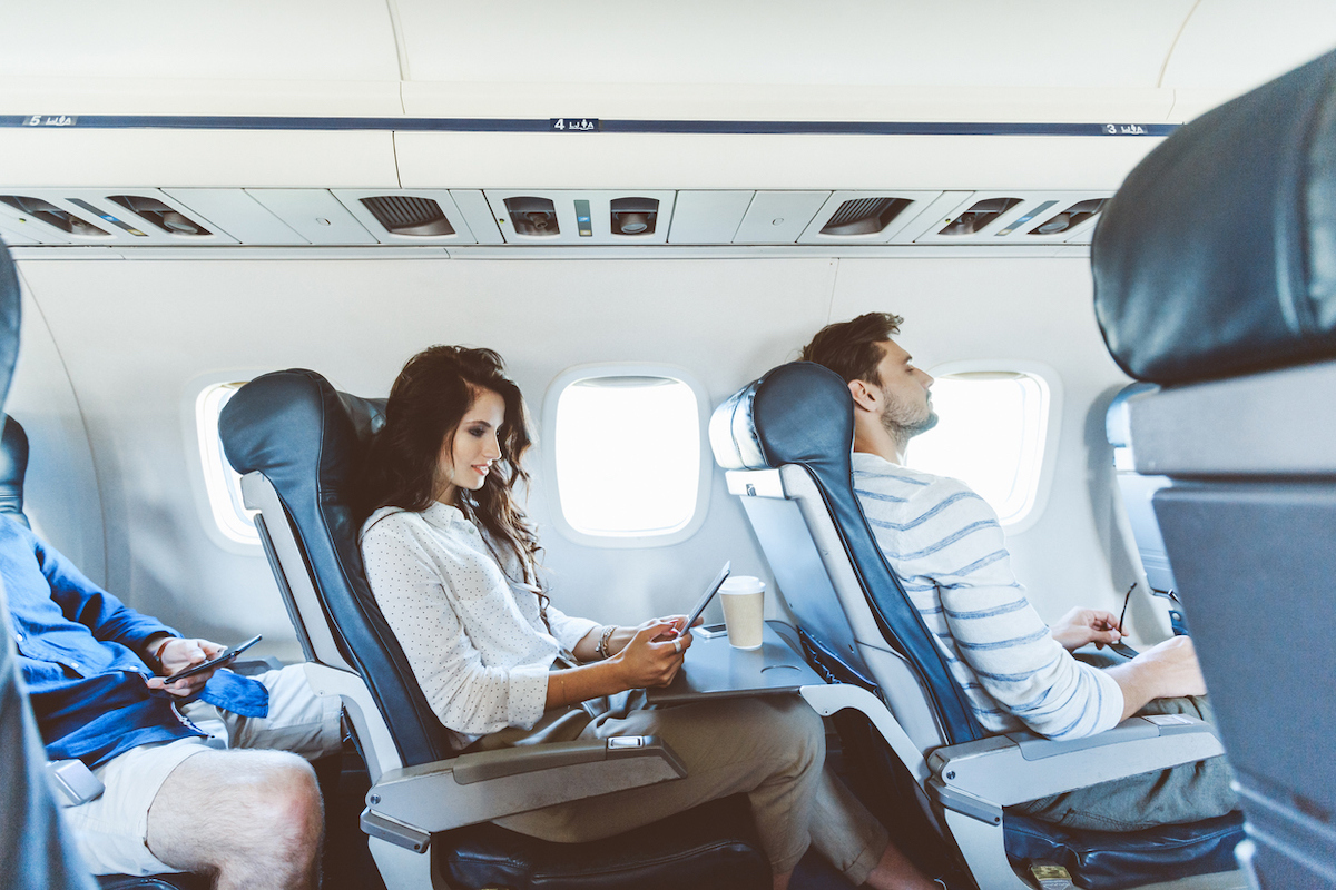 Young woman sitting in the aisle seat on an airplane using a digital tablet with two males on either side.