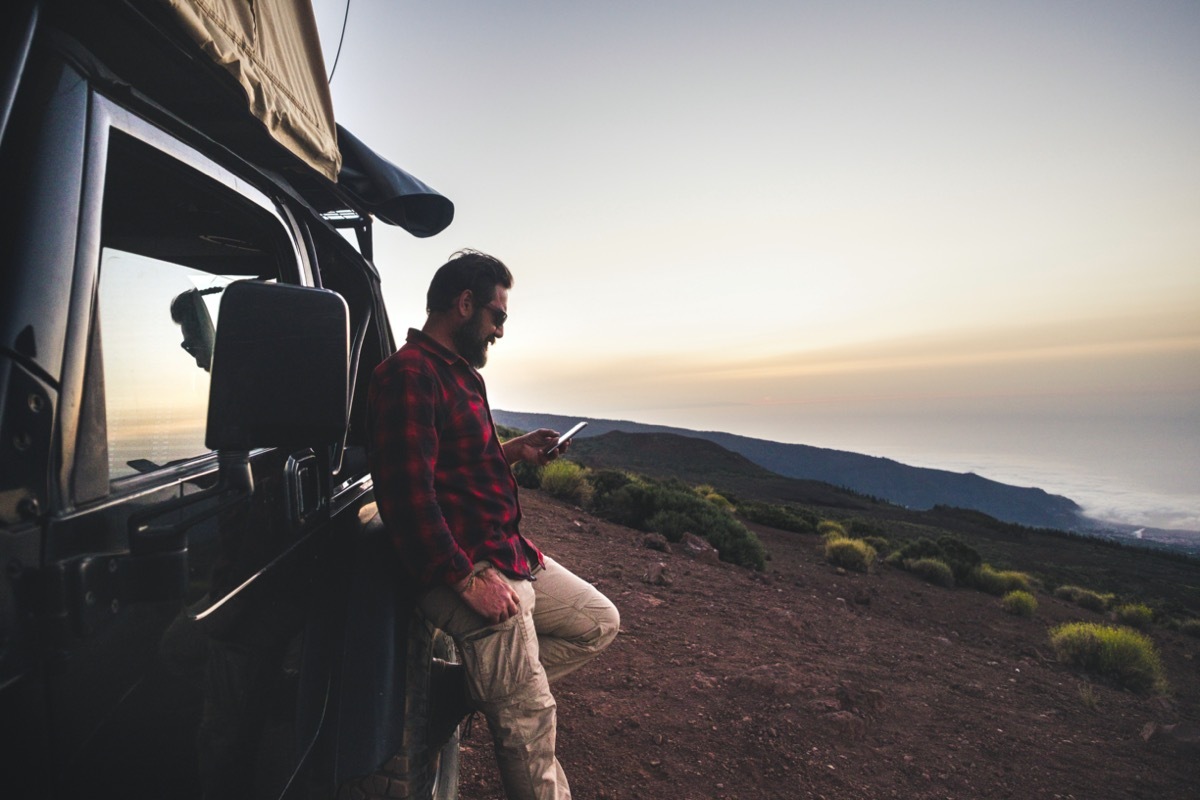 man leaning against truck standing against stark landscape at dusk