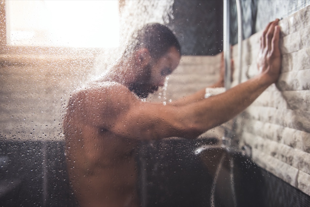 young black man leaning against shower wall with head in spray